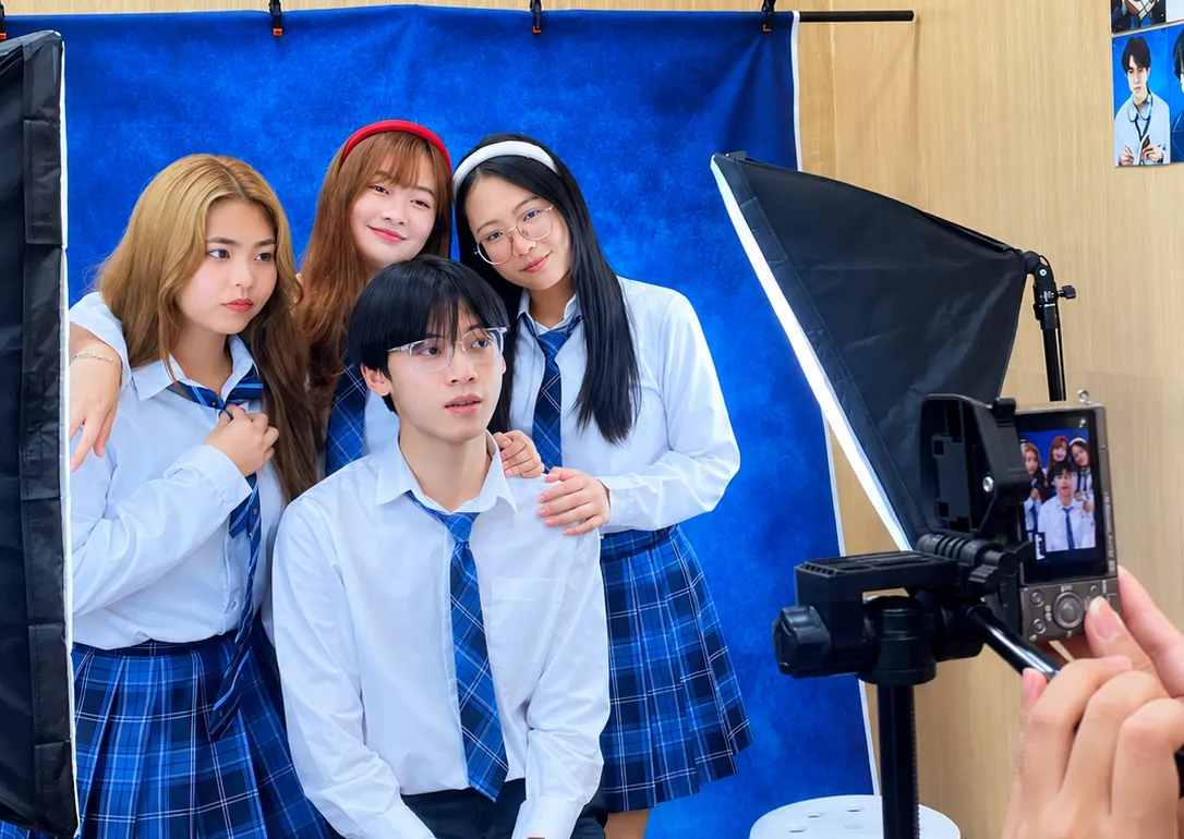 กลุ่มลูกค้าชุดนักเรียนโพสถ่ายรูปหน้าฉากสีน้ำเงินในบูธถ่ายภาพของ NK Board Game พร้อมกล้องและไฟสตูดิโอ